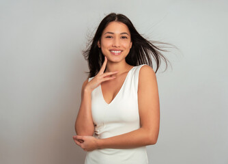 Beautiful young woman with long black hair posing in dress on grey background