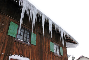 Fototapeta na wymiar Große gefährliche Eiszapfen und eine Dachlawine auf einem Hausdach im Winter