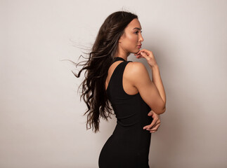 Fototapeta premium Beautiful young woman with long shiny black hair and natural make-up posing in dress on grey background 