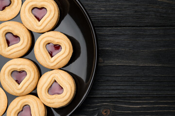 Cookies. Cookie Hearts shape Red jam or strawberry jelly inside biscuit cookie. Homemade baking. Sweet bakery. Top view on black background with copy space.