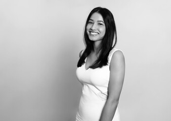 Beautiful young woman with long black hair posing in dress on grey background