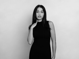 Naklejka premium Beautiful young woman with long black hair posing in dress on grey background