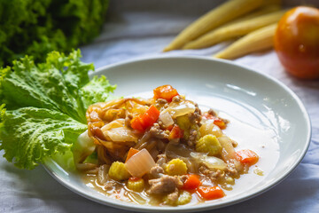 Flate noodle with minced pork sauce on a white plate on a white wooden table with baby corn and tomato and