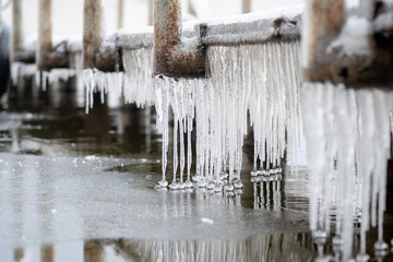 long icicles hanging from an icy pier with balls at the end near the water