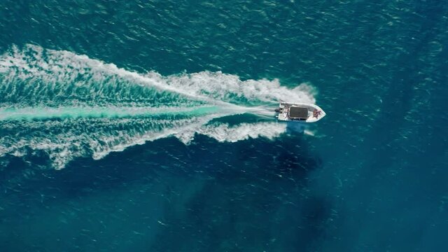 Scenic aerial shot of fast small white speed boat sailing straight leaving beautiful tail track and foaming waves behind. Clear blue sea background, copy space. Travel destination 4K. People on yacht