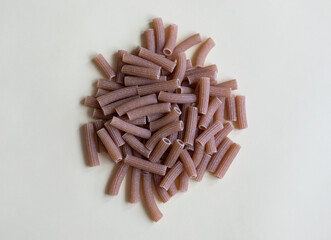 Raw whole grain brown pasta on a white background. Wholemeal pasta made of durum flour, rich in nutrients protein, carbohydrates and fiber