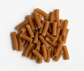 Raw whole grain brown pasta on a white background. Wholemeal pasta made of durum flour, rich in nutrients protein, carbohydrates and fiber