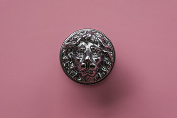 Solid metal silver coloured vintage style lion head handle against a pink painted door.
