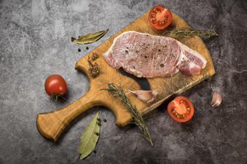Fresh meat, pork carbonate on a cutting board with tomatoes and spices on a gray mottled background