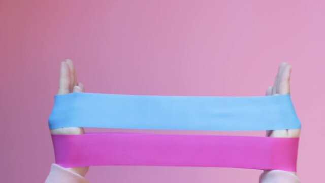 Girl holds two fitness gums, espander on pink background, front view