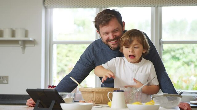 Father and son in pyjamas baking in kitchen at home following recipe on digital tablet - shot in slow motion