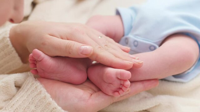 Closeup of woman gently stroking with hand tiny feet of her newborn baby son with perfect skin. Concept of family happiness and loving parents with little children