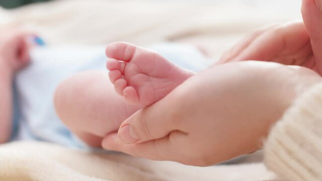 Tiny baby feet in female hands. Young mother gently touching and stroking her newborn baby legs. Concept of family happiness and loving parents with little children.