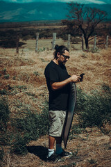 Vertical de un Hombre con gafas en el campo utilizando el celular mientras sostiene un reflector