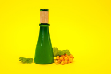 Green glass bottle covered with wooden cap filled with natural vegan-friendly cosmetic product on yellow background, berry Hippophae, copy space for advertising