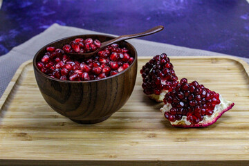 Red pomegranate seeds close up in a wooden bowl with a wooden spoon. Two pieces of pomegranate with ripe red seeds on a wooden tray.