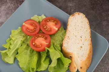Tomatoes on lettuce leaves with French baguette on a rectangular plate