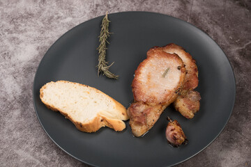 Roast pork loin, on a round plate, with rosemary garlic, on a gray background