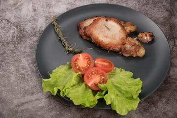 Roast pork loin, on a round plate, with lettuce, rosemary and tomatoes, on a gray background