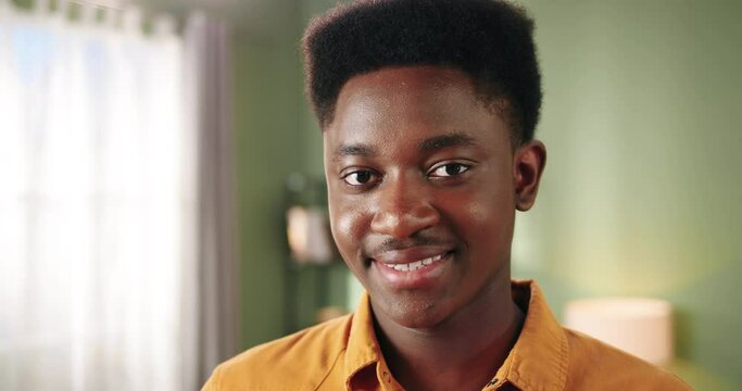 Close up of handsome cheerful young African American man looking at camera and smiling in positive mood alone in room in house. Afro guy posing with smile on face at home. Emotions concept