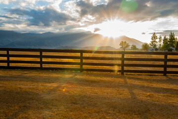 Fototapeta premium Post and rail fence across farm backlit by setting sun