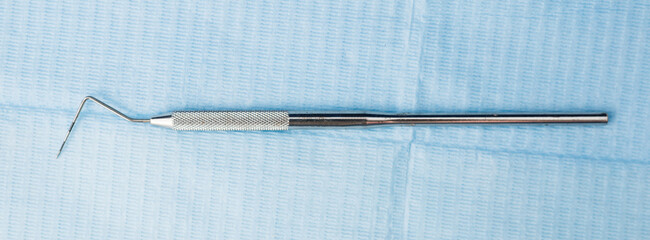 Closeup of stainless steel dental explorer or sickle probe on background of blue napkin....
