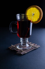 Hot mulled wine in a tall glass mug with orange straws on a dark background with copy space