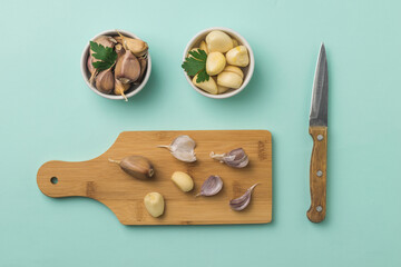 Cutting board with peeled and unpeeled garlic and a knife on a blue background.