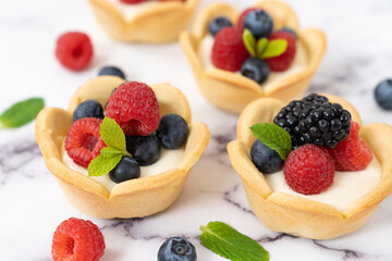 Delicious pastry mini fruit cream cheese pies or tart cakes with fresh raspberry, blueberry and blackberry