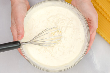 Mix of cream cheese, milk and mozzarella cheese in a bowl, and raw lasagna noodles close up. Step...