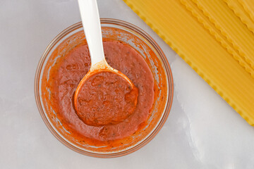 Lasagna noodles and bowl of marinara sauce close up on marble background directly from above