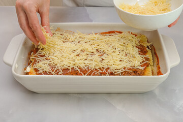 Topping lasagna with parmesan cheese. Step by step beef lasagna recipe. Front view, woman hands, marble background