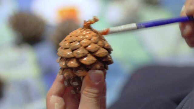 Close up on caucasian boy's hands , holding a brush, painting a pine cone for Christmas