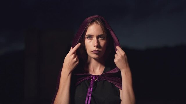 Mysterious woman wearing a purple cape slowly putting the hood over her head and staring at the camera. Fantasy cosplay concept