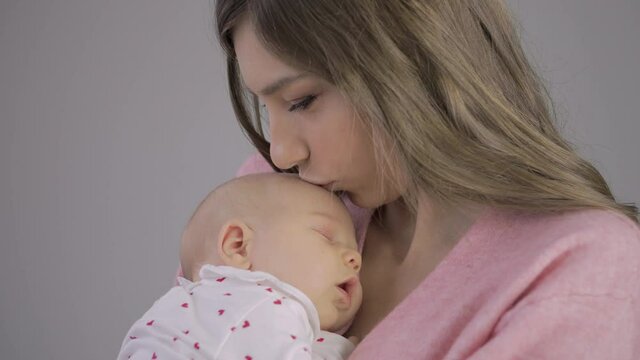A young mother gently kisses her newborn baby on the head.