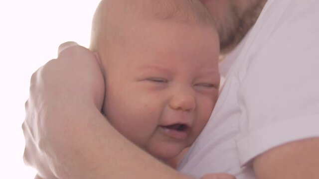Close-up of a crying baby's face as the father tries to console his child.
