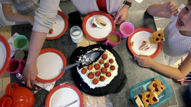 Family celebrating with strawberry cake. Coffee during Swedish school graduation. Woman cuts a piece of cake. Overhead shot.