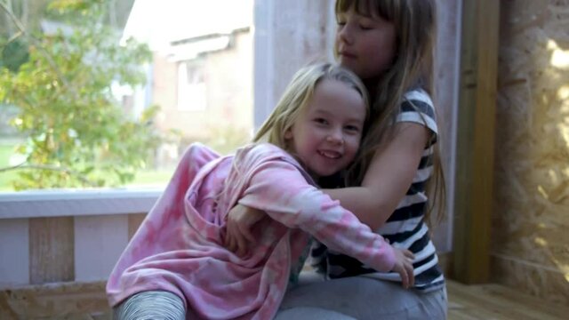 Two girls hugging. One holds on to tease the other. Typical sibling love. Soft light in playhouse and captured in a natural real situation.