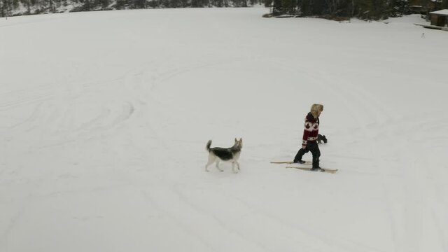 Adult man in large fur hat, walks and plays in traditional snowshoes on frozen lake with his pet dogs in northern Canada.