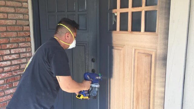 Portrait of professional painter using airless sprayer to paint house doors with primer