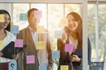 Happy smile asian business people woman, man post sticky notes on glass wall, share ideas, plan, project with team colleague or coworker, meeting in office. Brainstorming business teamwork concept.