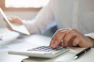 Fototapeta premium Close up hand of young asian businessman is pressing a calculator to calculate cost from book bank to plan his spending for payday.