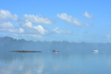 Fototapeta na wymiar Hazy morning in calm harbour. Sky reflection on calm surface gives blue look to whole image.