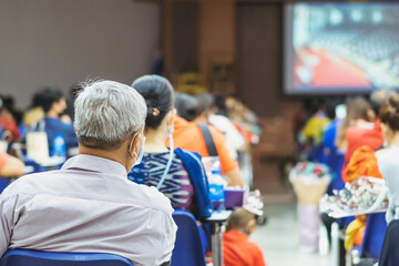 Back view of Asian man wear protective face mask to prevent Coronavirus(COVID-19) sitting on a chair for social distancing in  auditorium. Conference concept in coronavirus pandemic.Selective focus.