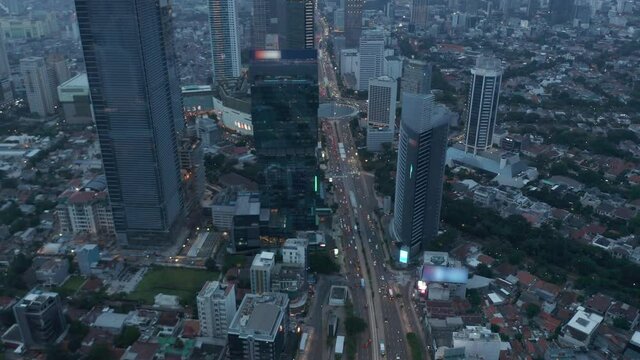Aerial dolly shot of vehicles on a busy multi lane road and roundabout at dusk in modern city center in Jakarta, Indonesia with no Company Logos