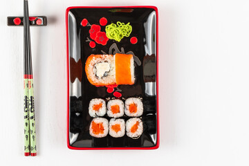 fresh appetizing philadelphia rolls with salmon and soft cheese in black red plates on a white background