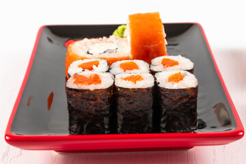 fresh appetizing philadelphia rolls with salmon and soft cheese in black red plates on a white background