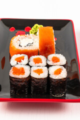fresh appetizing philadelphia rolls with salmon and soft cheese in black red plates on a white background