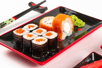 fresh appetizing philadelphia rolls with salmon and soft cheese in black red plates on a white background