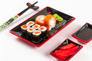 fresh appetizing philadelphia rolls with salmon and soft cheese in black red plates on a white background